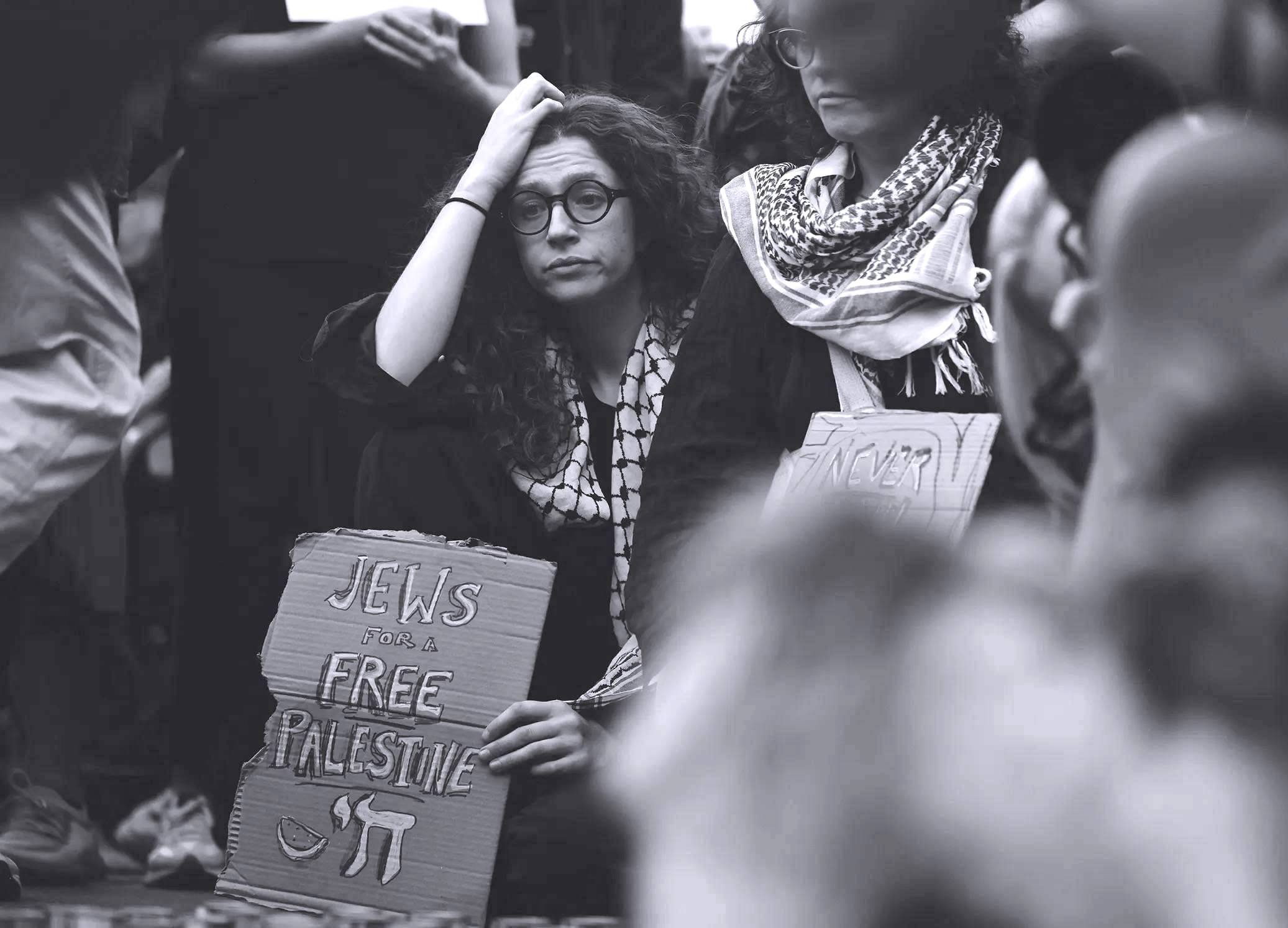 Protesters in keffiyehs look dejected. One holds a sign reading "Jews for a Free Palestine. Source photograph by Michael M. Santiago / Getty