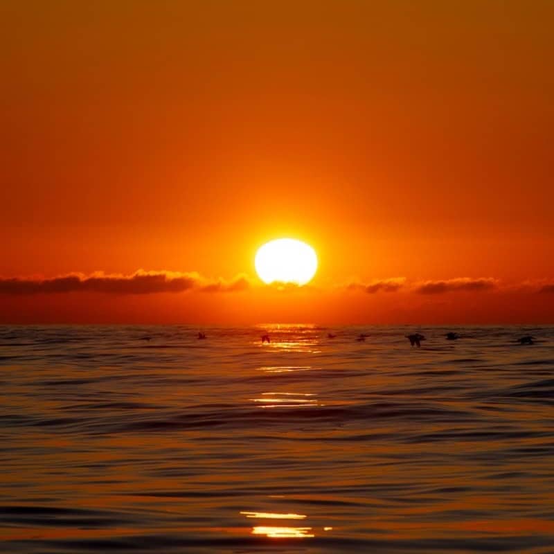 Sunset over the ocean, bathed in orange glow.