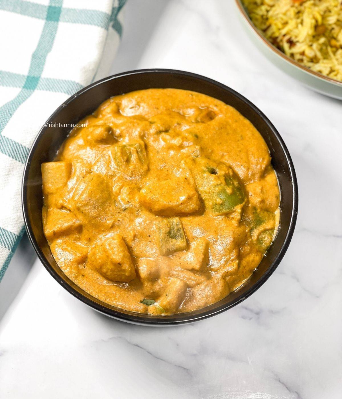 A bowl of potato Tikka masala curry is on the marble table.