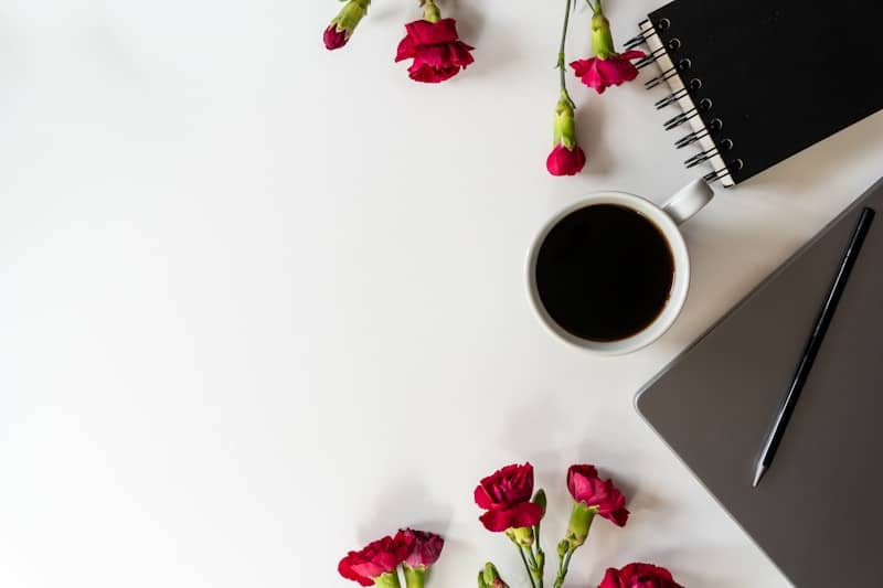 Red carnations, coffee, notebook, and laptop on a white desk