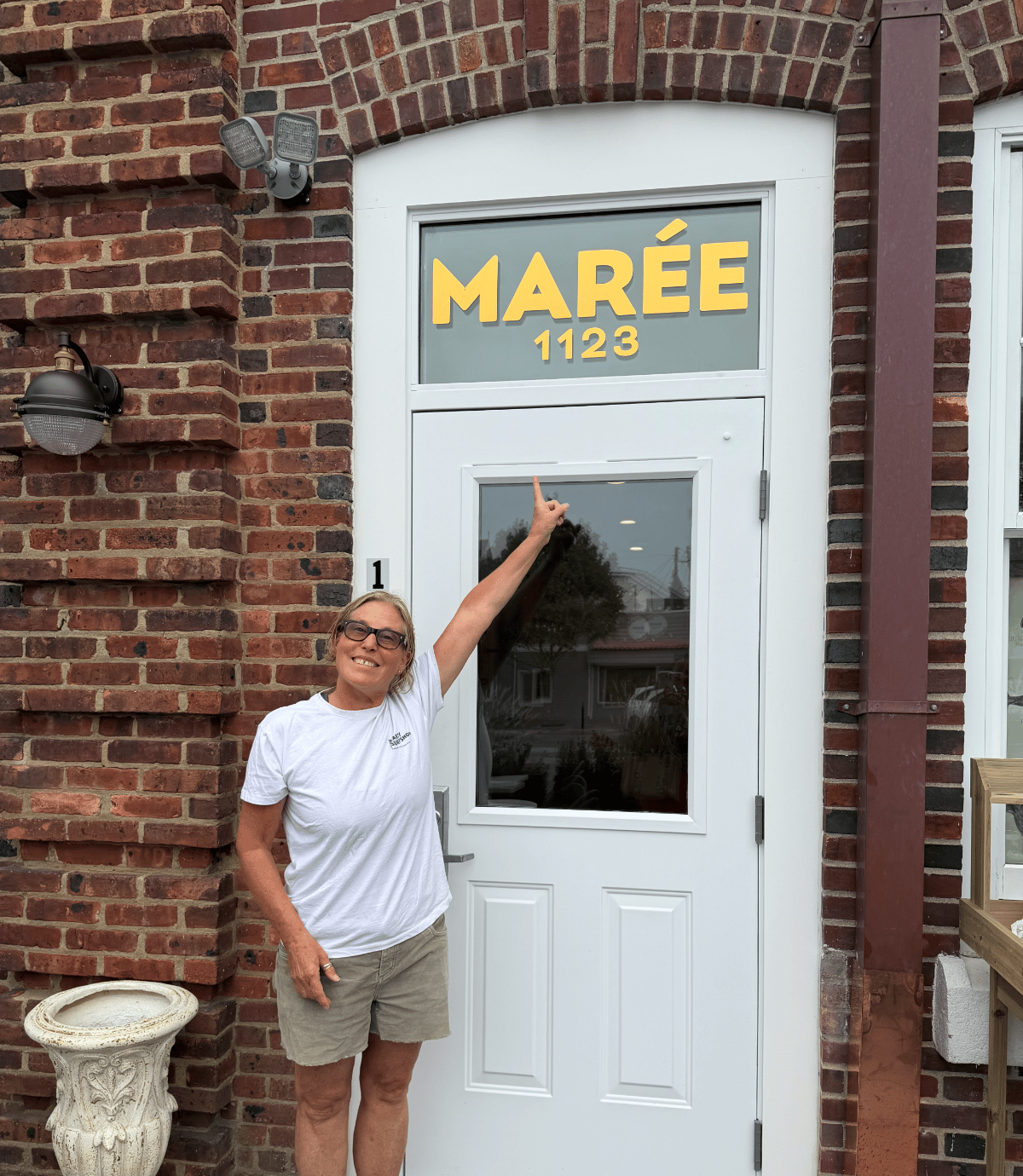 A member of the Marée team pointing up at the MARÉE 1123 sign above the front door