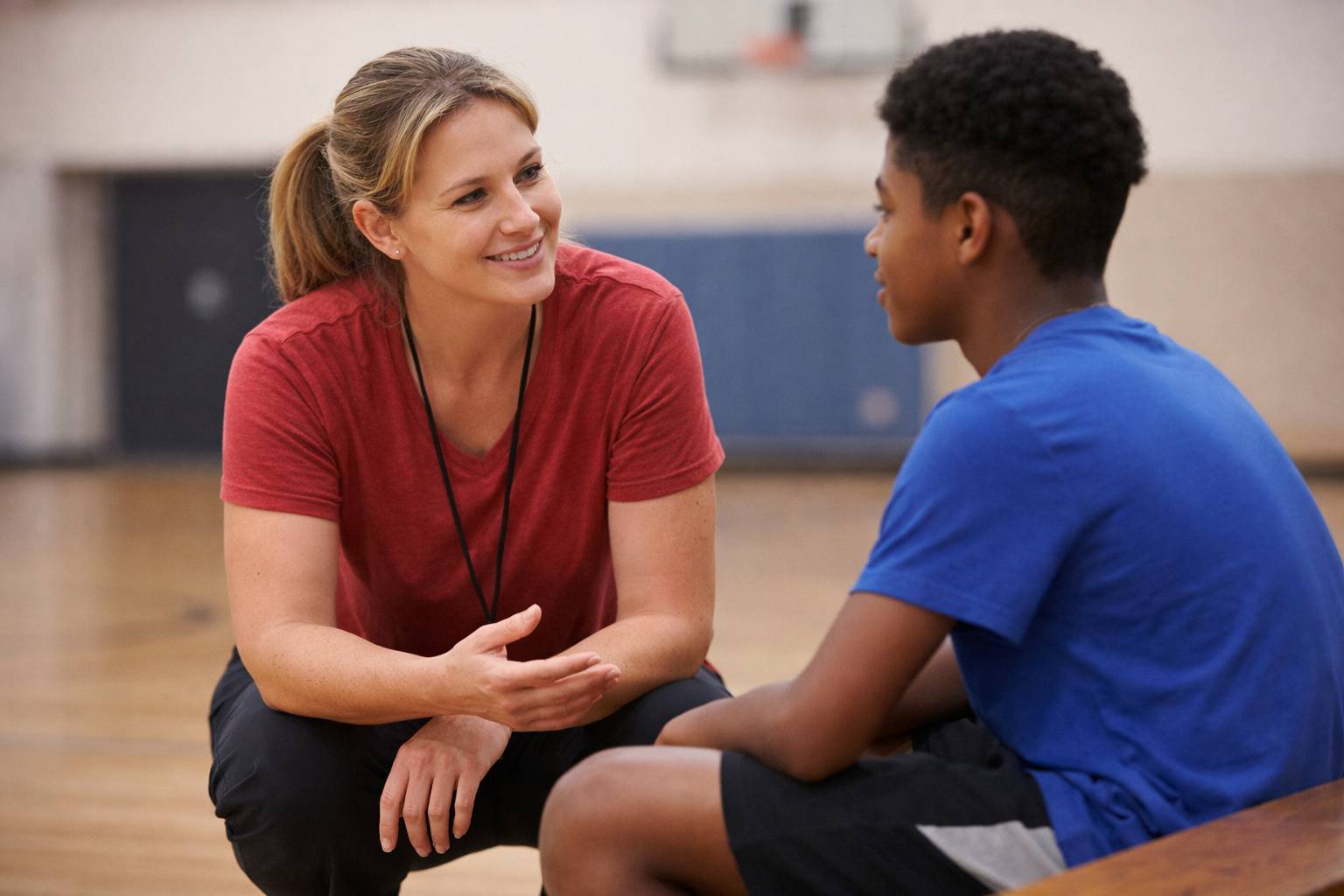 Physical education teacher having a supportive one-on-one conversation with a student in a gymnasium.