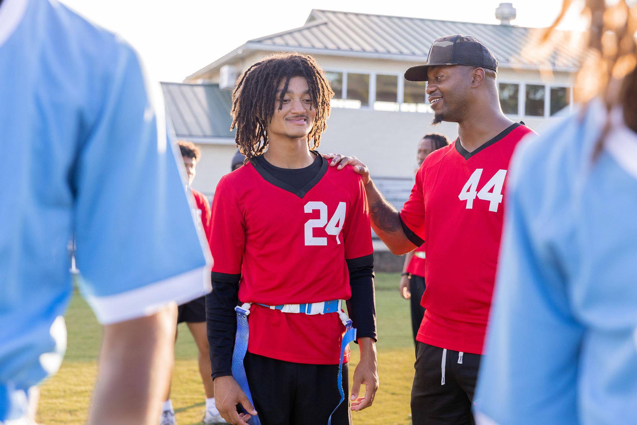 PE teacher speaking with a student during a flag football game while other players stand nearby on the field
