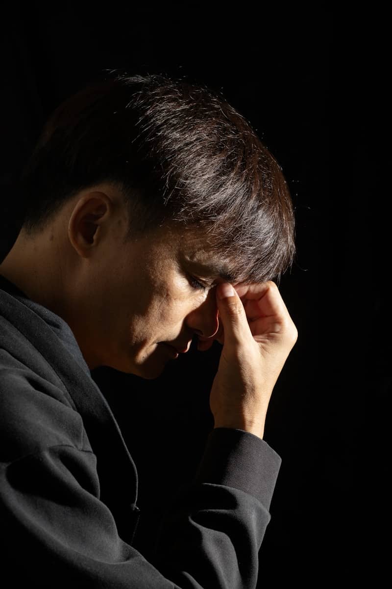A man in dark clothes holds his forehead in thought