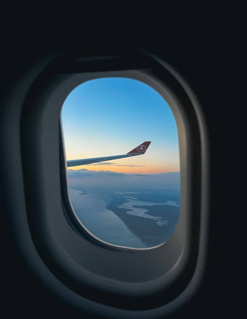 An airplane wing with a Turkish Airlines logo seen through a window above clouds