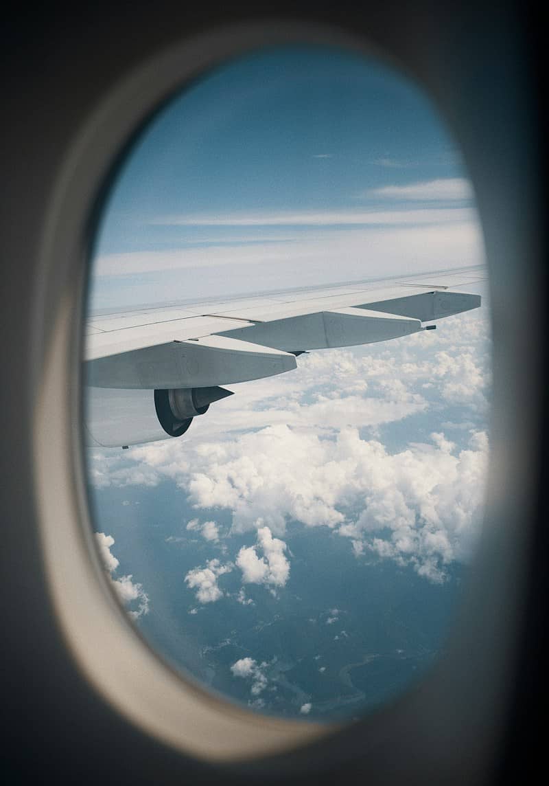 An airplane wing and engine seen through an oval window above white clouds