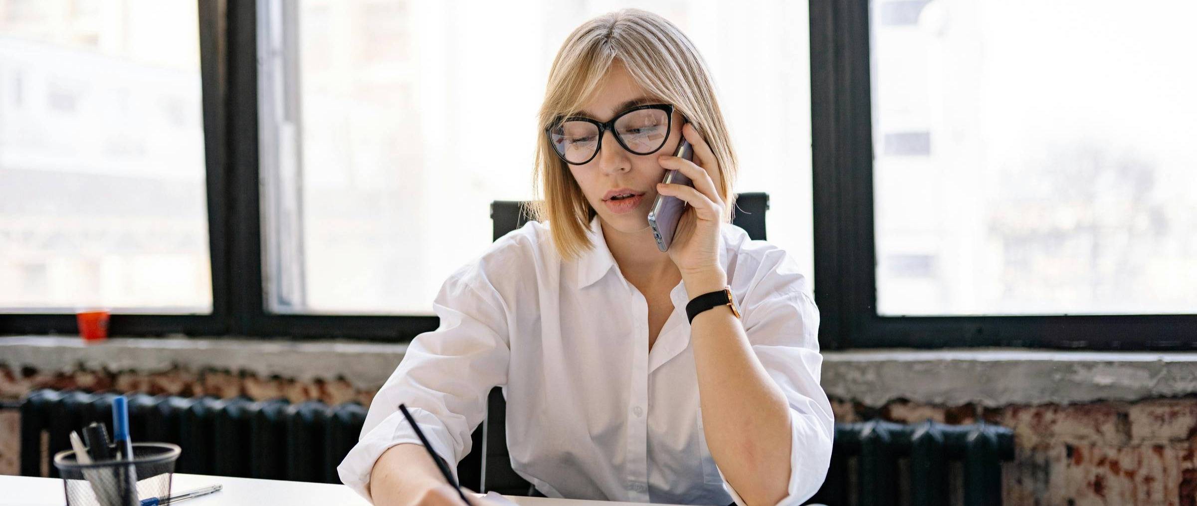 woman on phone at work writing down notes