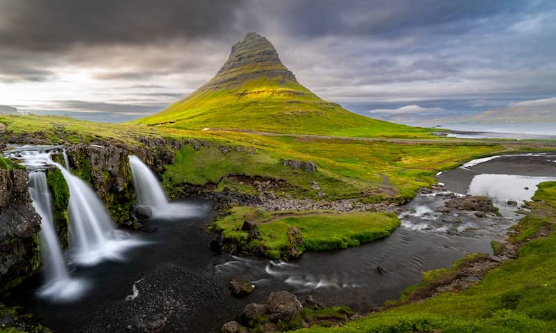 Green mountain with waterfalls under cloudy sky