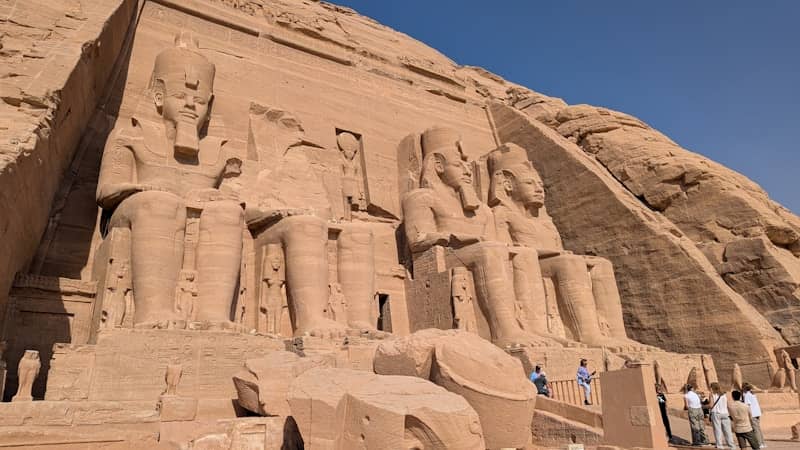 Massive ancient statues carved into a sandy cliff face.