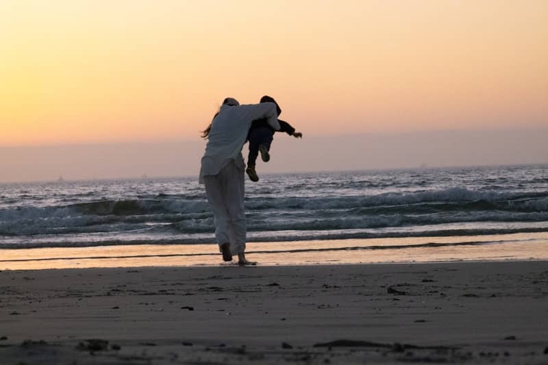 Father holding a child on the beach at sunset.