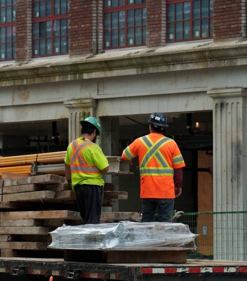 Two construction workers on a truck with lumber.