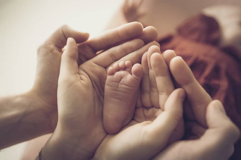 Parental hands cradle a newborn baby's tiny foot