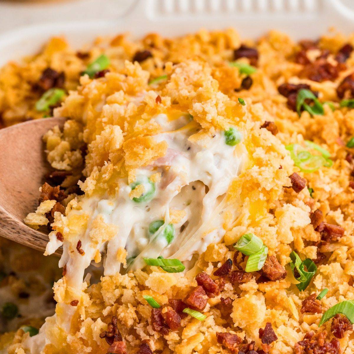 Scooping out a serving of a creamy chicken casserole topped with cracker crumbs, green onions, and bacon.