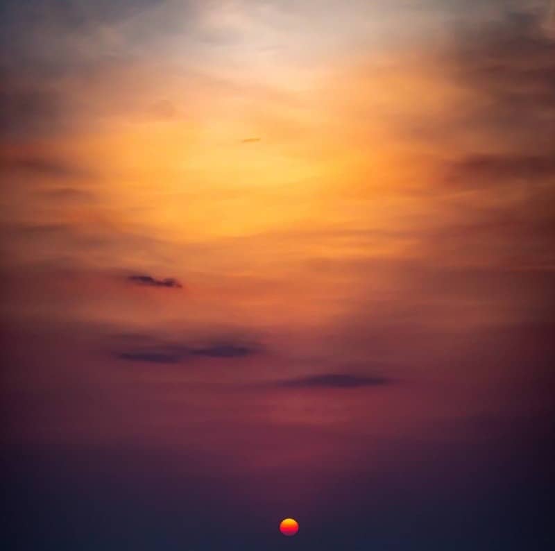 Sun setting over hazy mountains with warm orange and purple skies