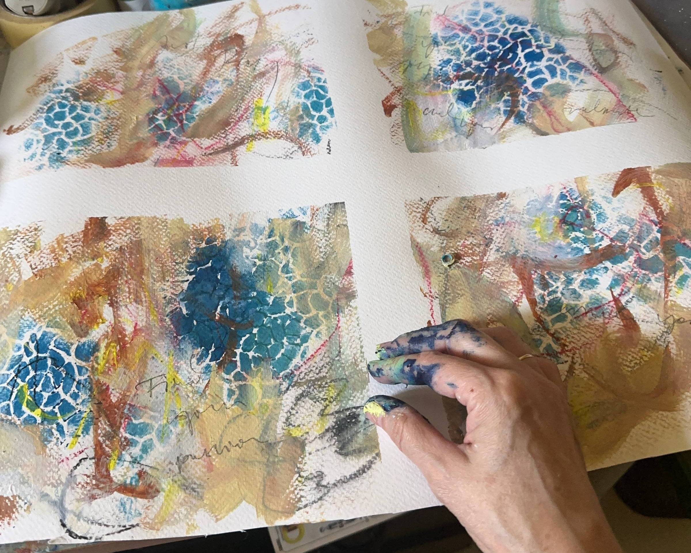 A hand resting on textured paper covered with soft layers of paint and handwritten marks.