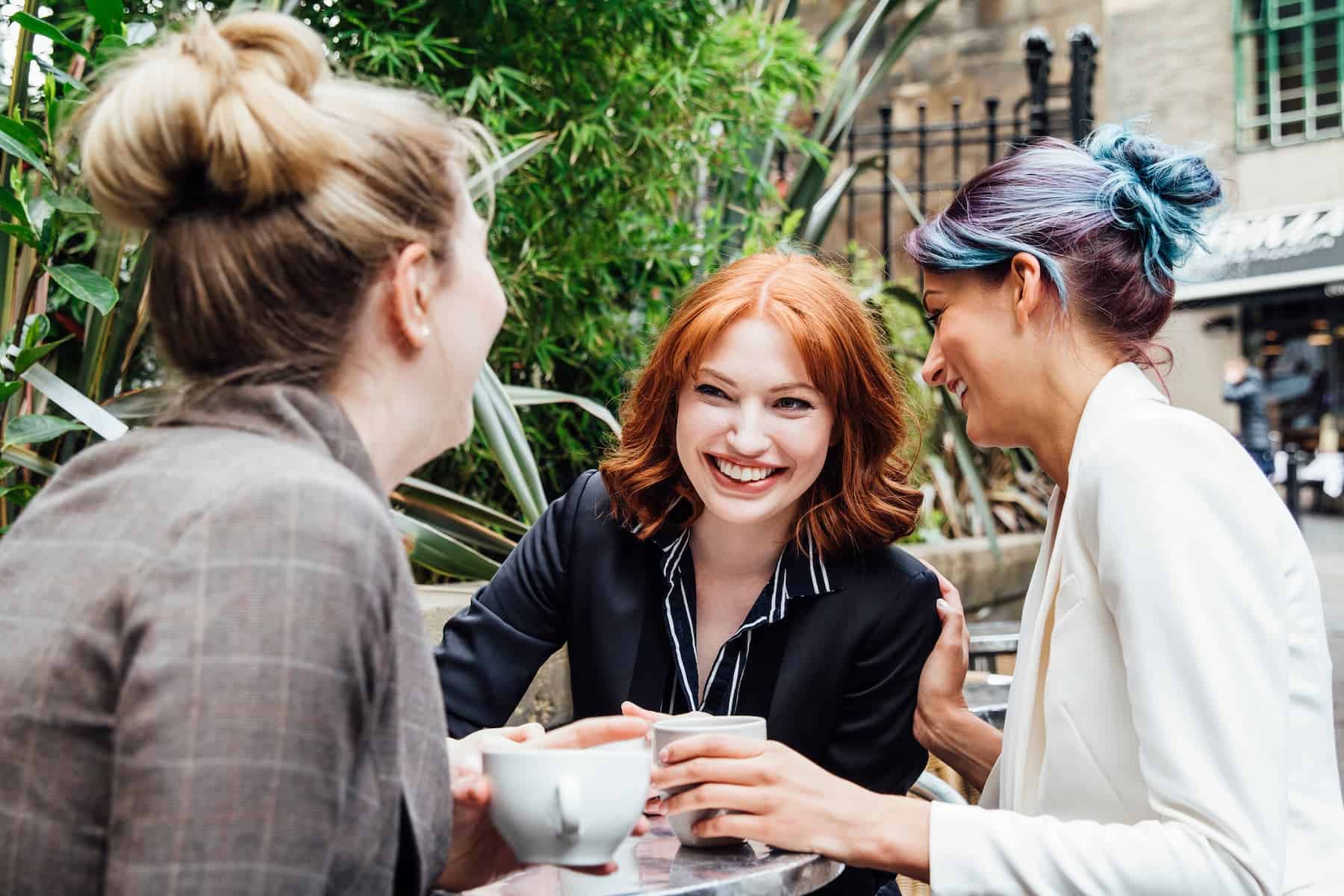Three people laugh together while sharing drinks outdoors — a warm reminder that an attractive personality is about positivity and genuine connection.