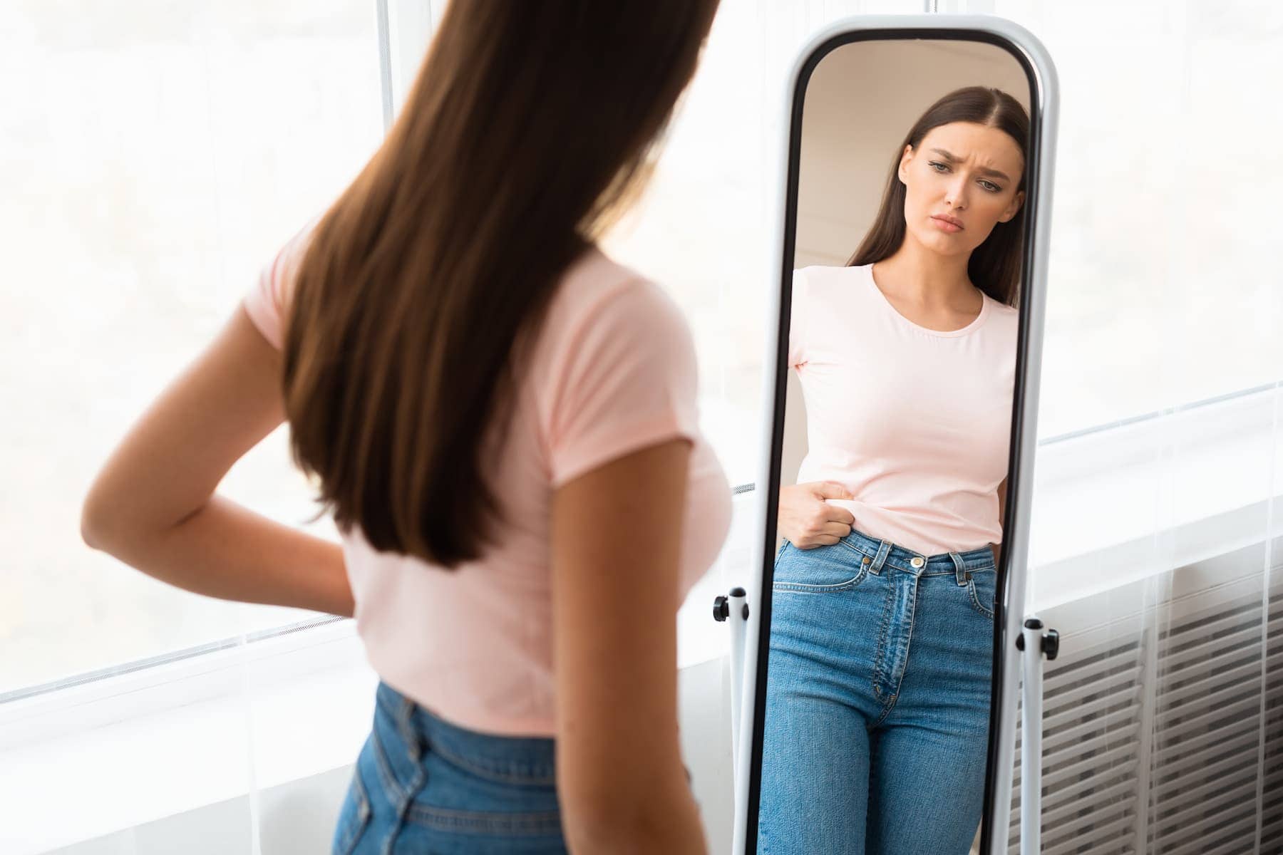 Looking unsure in front of the mirror, a woman feels frustrated not knowing how to dress for her body shape.