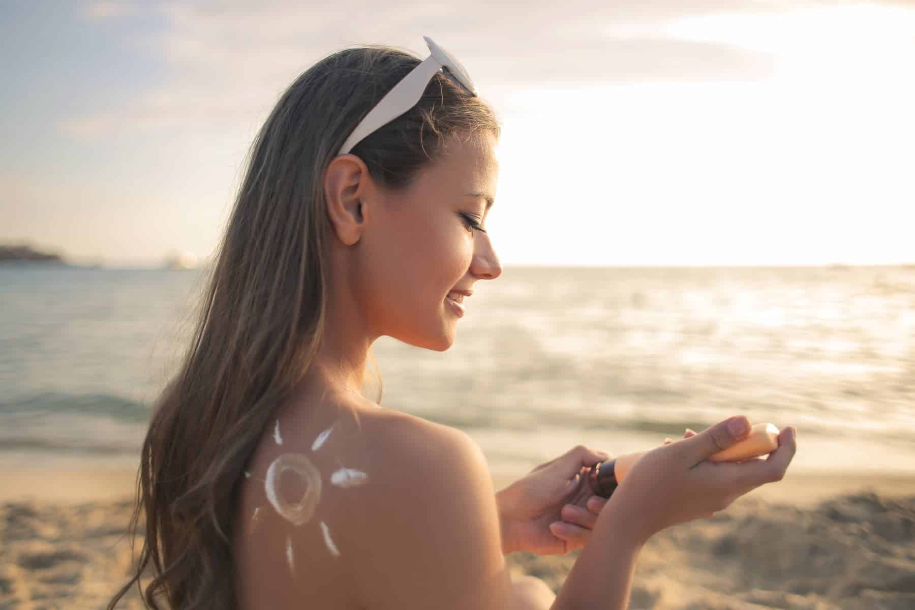 A young woman who understands the importance of protecting her skin from sun damage will apply sunscreen before basking in the sun at the beach.