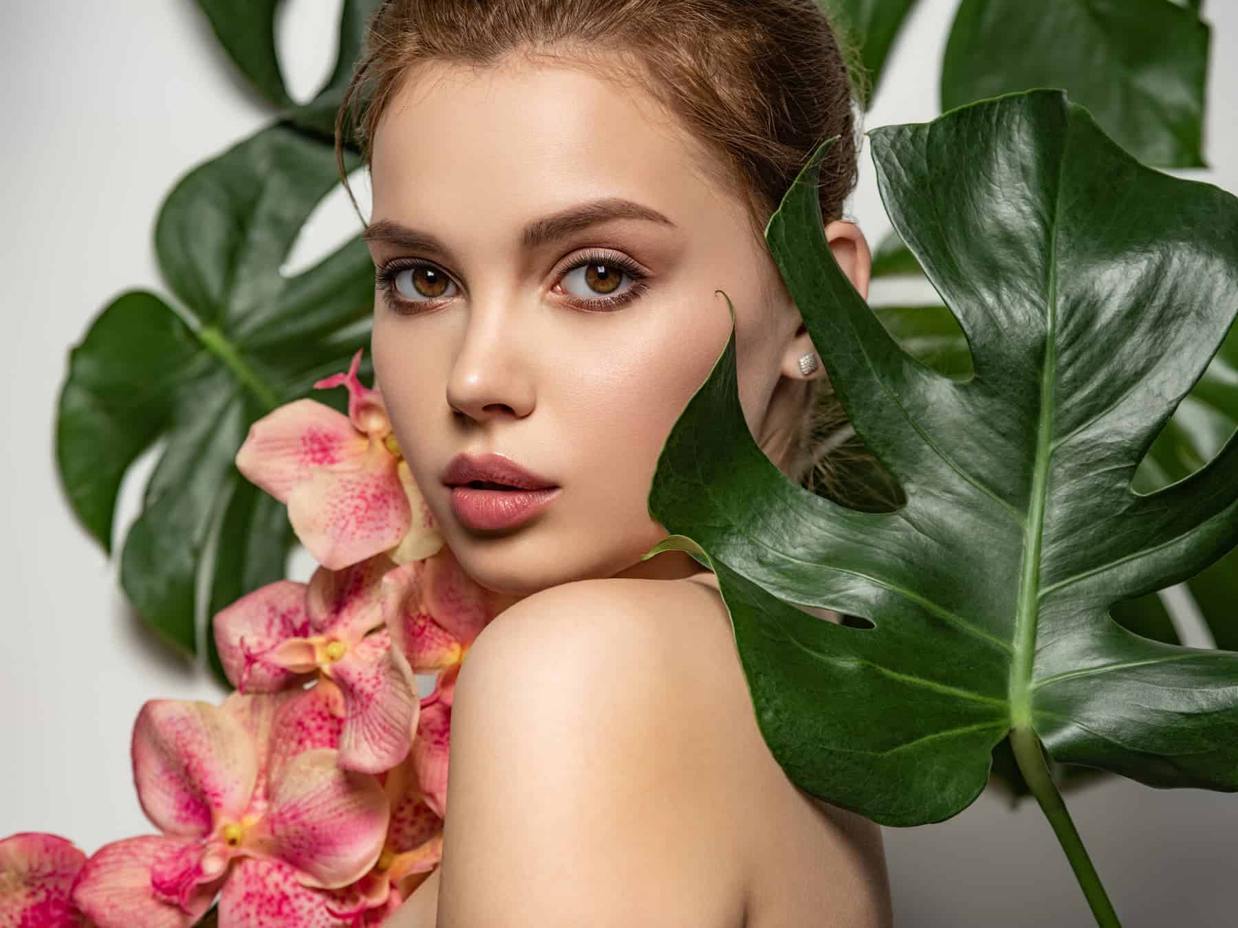 A beautiful woman with glowing skin poses among palm bushes, subtly promoting the idea that flawless skin requires an overuse of skincare products.