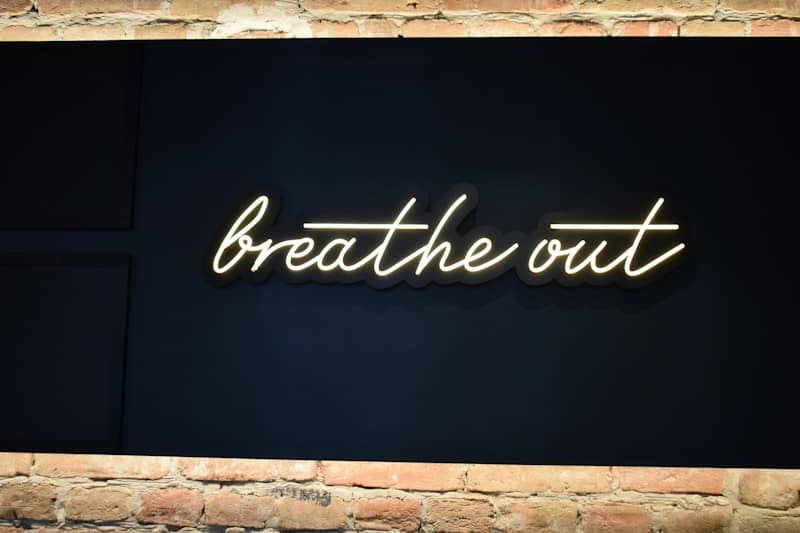 A neon sign reading "breathe out" on a dark panel above a brick wall
