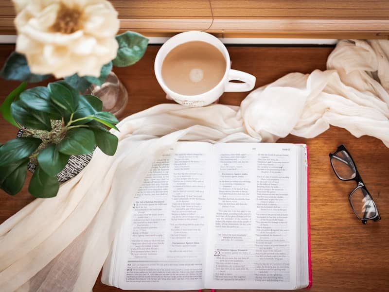 Open Bible with coffee and glasses on table.