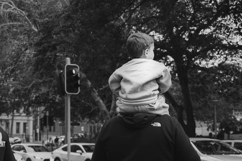 Child sits on father's shoulders looking at traffic light.