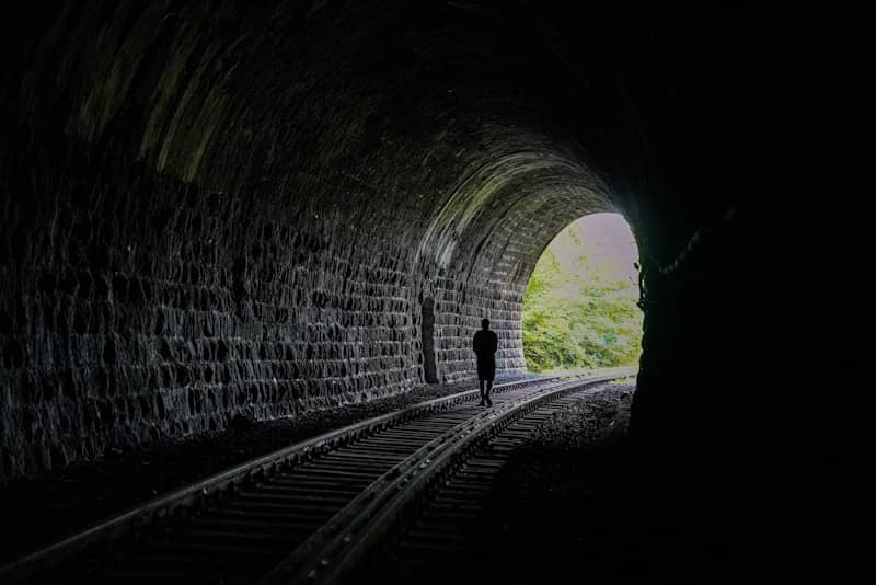 A person walking into a dark tunnel with a light at the end