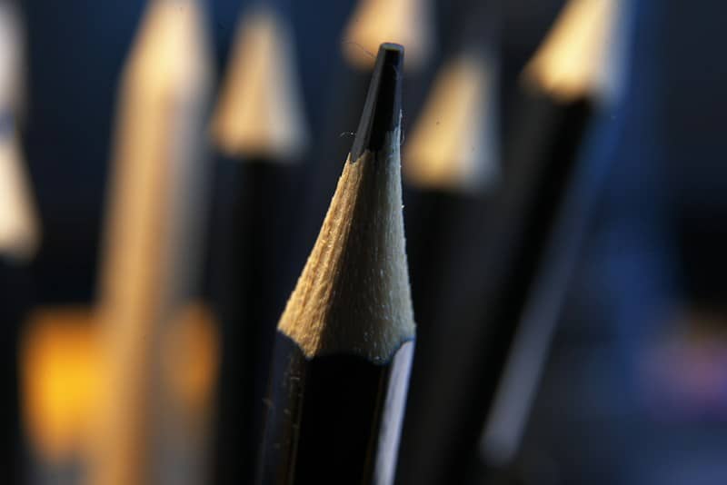 A sharpened black pencil in focus with blurred pencils in the background