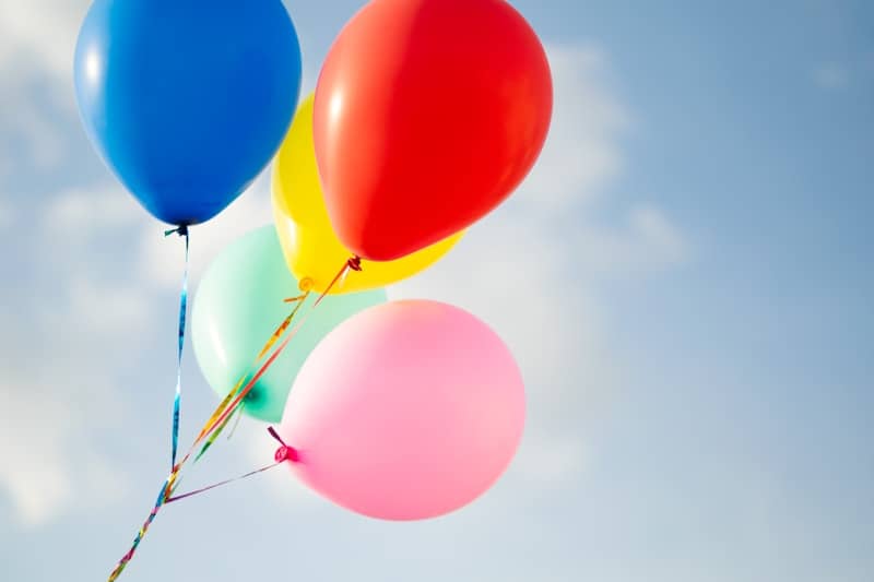 Colorful balloons float against a bright blue sky.