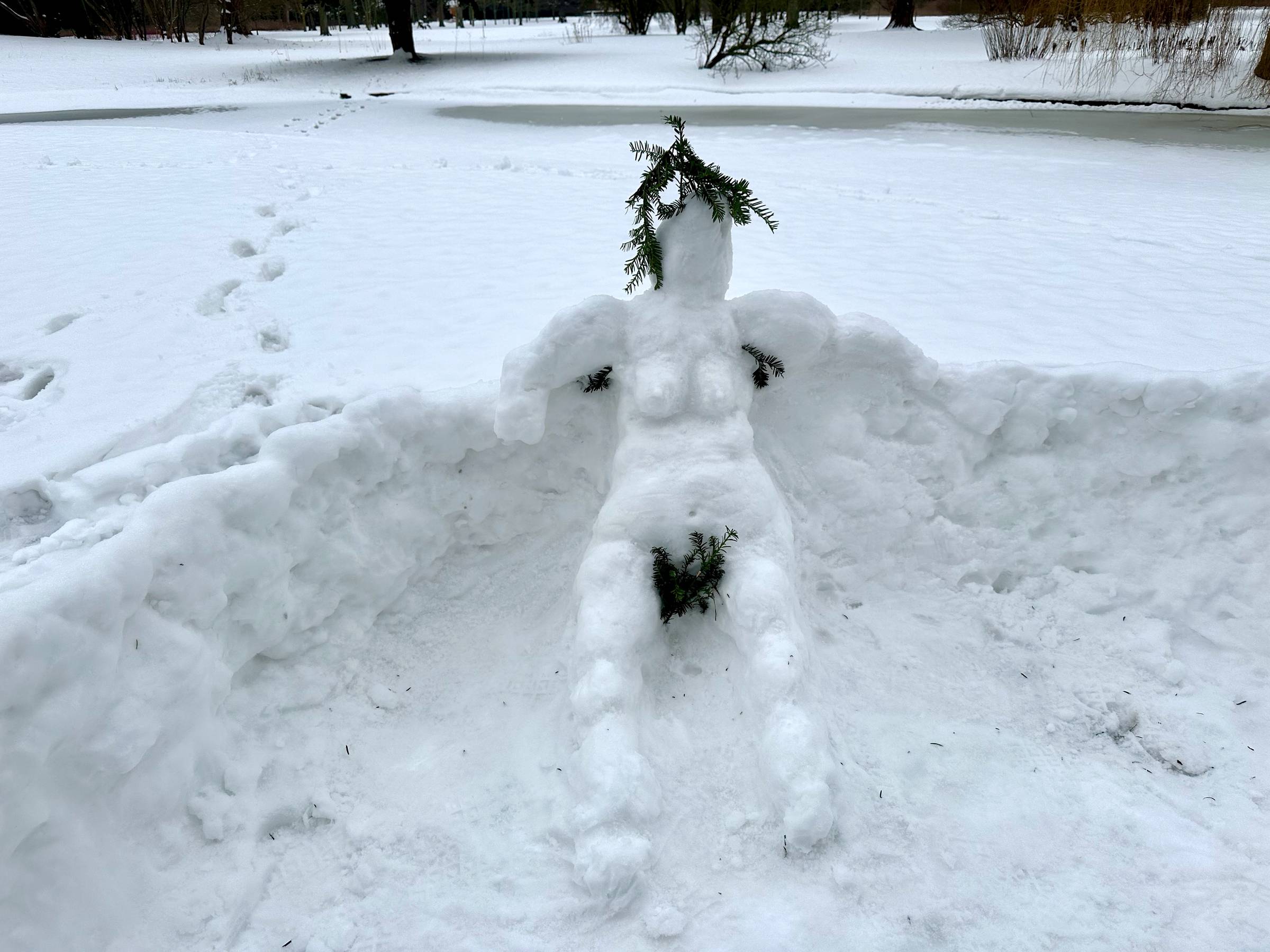 A snow sculpture of a woman with branches for hair, armpit and pubic hair. 