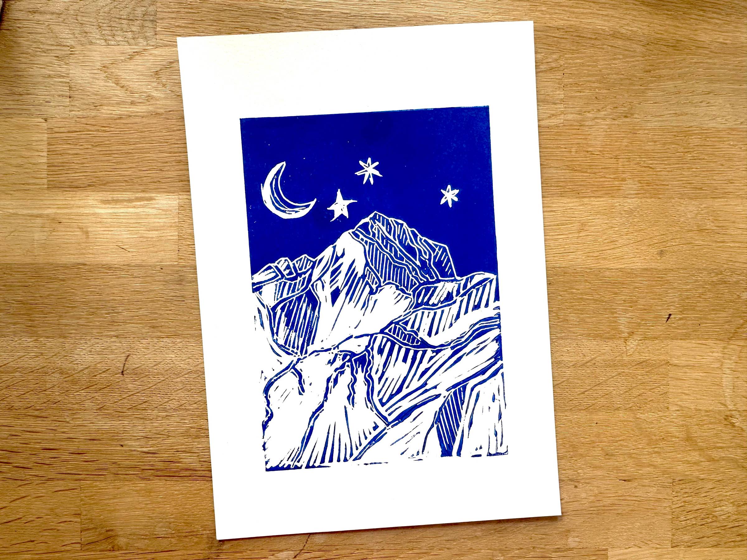 A lino printed illustration of Triglav, Slovenia's highest mountain with the crescent moon and stars above it.