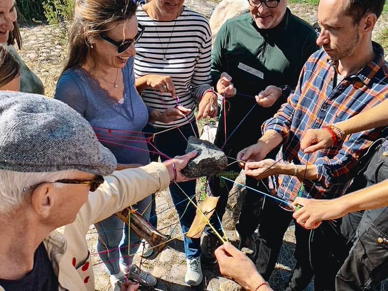 A group of people holding the web of strings with their hands while balancing a stone on it.