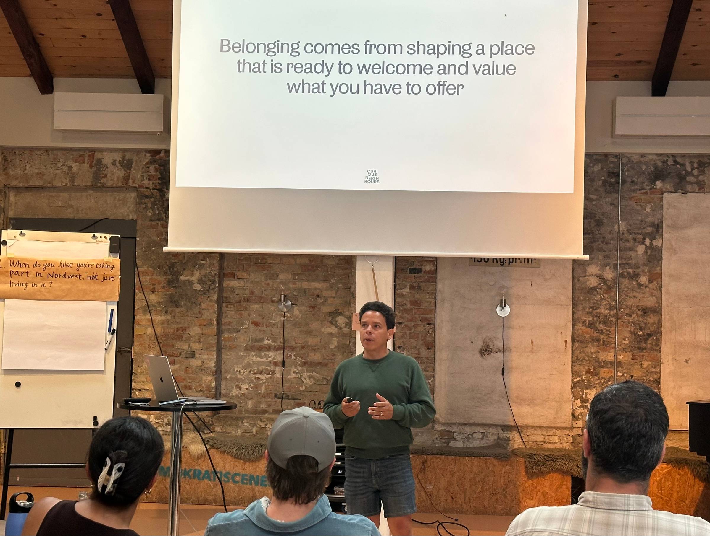 Image of Gus Guerrero with a slide behind him showing a statement: "Belonging come from shaping a place that is ready to welcome and value what you have to offer."