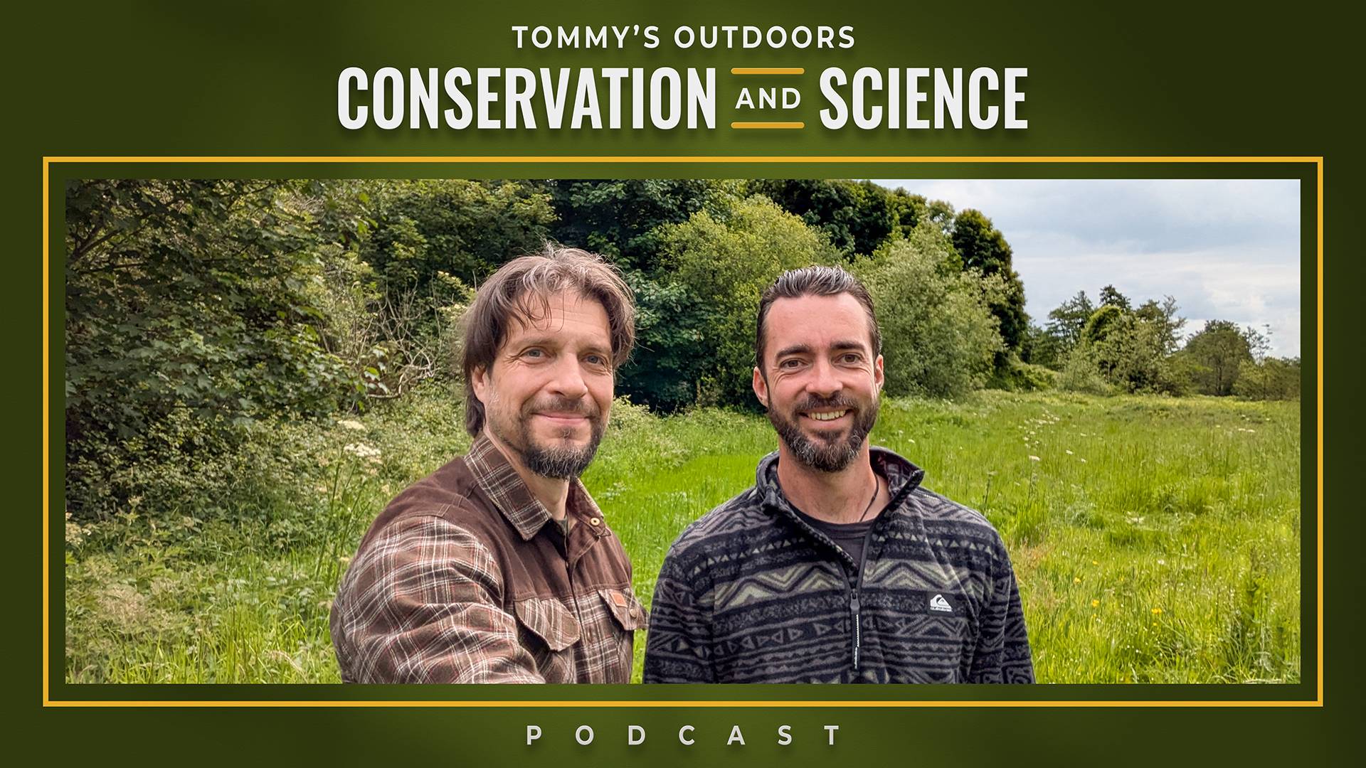Two men standing in a lush green meadow with dense woodland in the background under an overcast sky. The guest on the left has shoulder-length brown hair and a beard, wearing a brown and cream chequered flannel shirt. The podcast host on the right has short dark hair and a beard, wearing a dark patterned fleece jacket. Both men are smiling at the camera in what appears to be a natural countryside setting with tall grass and mature trees creating a scenic outdoor backdrop.