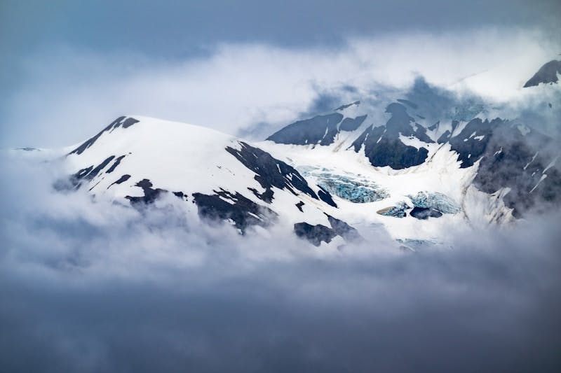 A mountain covered in snow and clouds under a cloudy sky