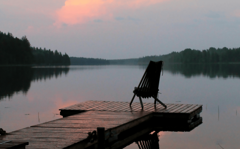 empty wooden chair facing a calm lake at sunset, a quiet image of loneliness and grief after losing a parent