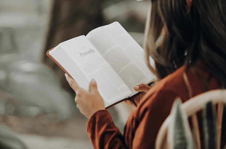 A woman in an autumn colored top reading an open Bible, searching for comfort and bible verses for losing a parent in the quiet moments of grief.
