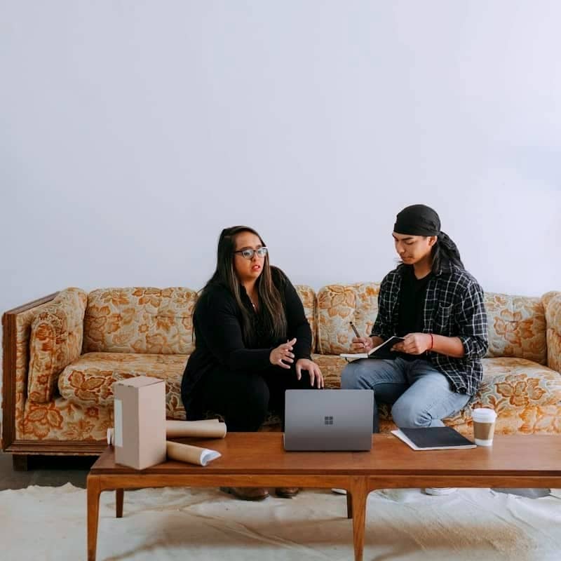 two people sitting on a couch looking at a laptop