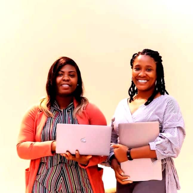 Two women standing next to each other holding laptops