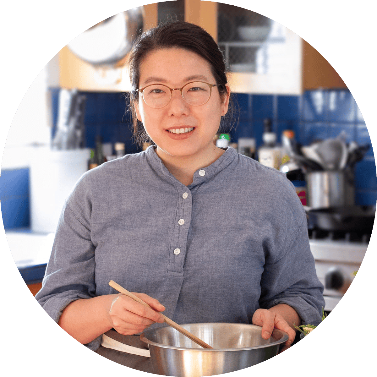 Cindy holding chopsticks and a mixing bowl while smiling in a kitchen.