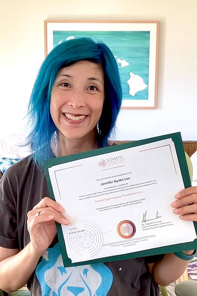 Jenn holding a Somatic Experiencing Practitioner Certificate and smiling