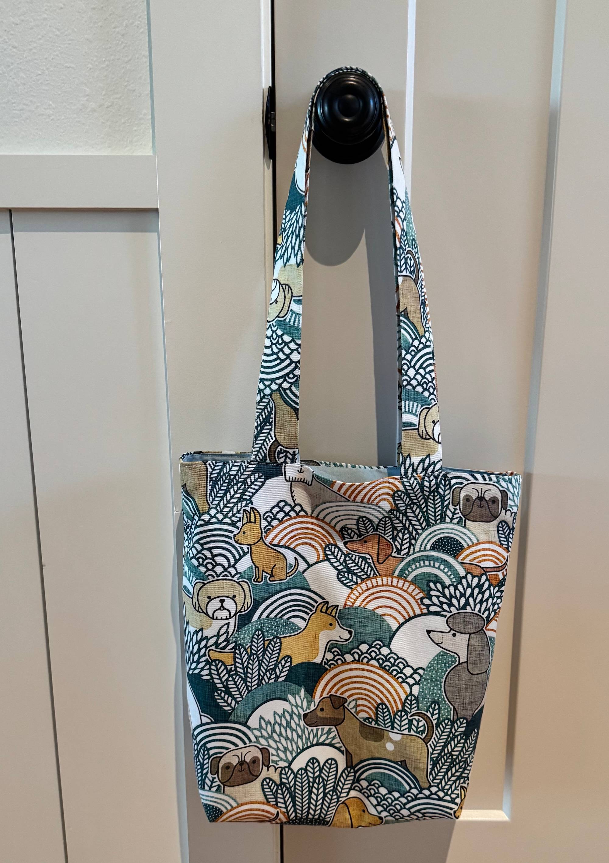 A bag with a graphic pattern of illustrated dogs in a botanical setting. The bag is hanging from a door knob.