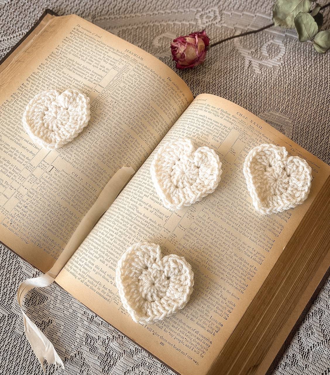 Cream crochet hearts on a vintage book with a pink dried rose in the background