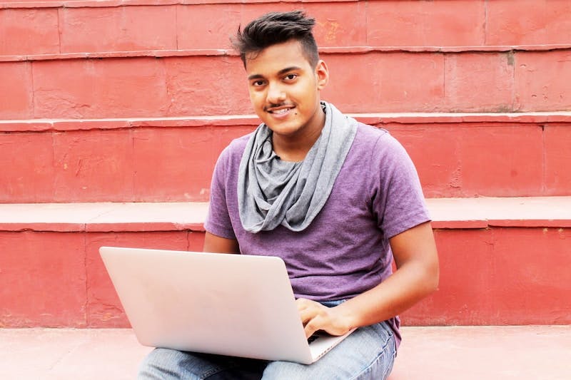 Portrait of a young man sitting outside with a laptop. He's looking at the camera. 