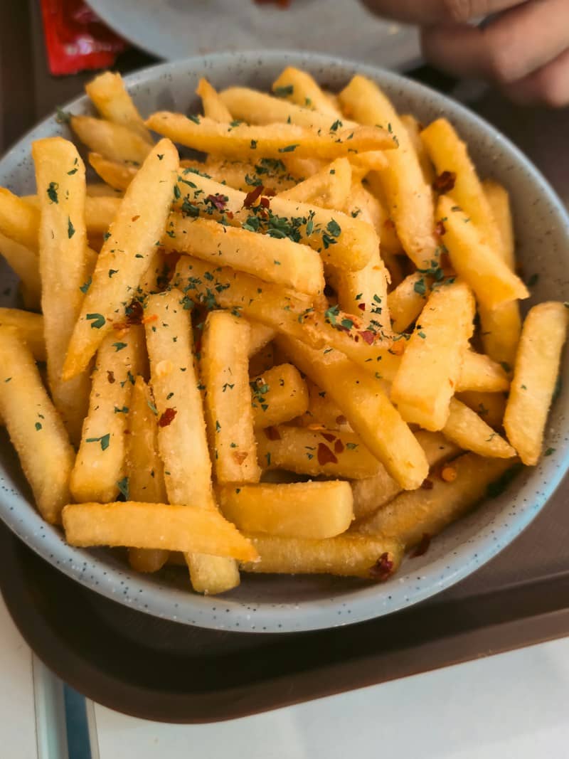 A bowl of golden french fries topped with green herbs and red chili flakes