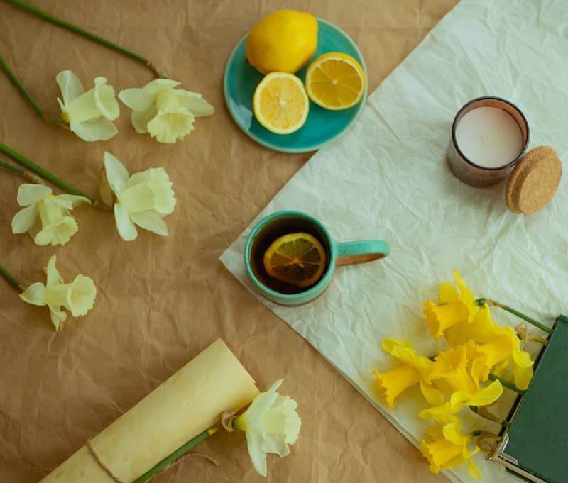 a table with a green cup of tea, a sliced lemon, and yellow and white daffodils