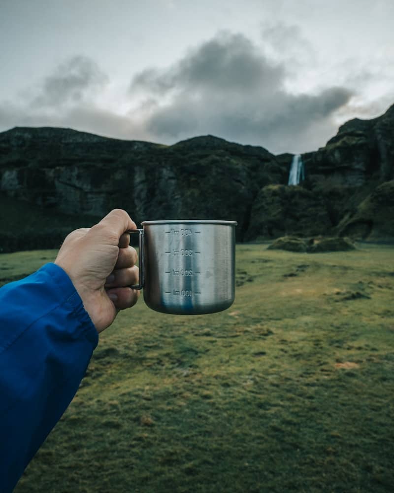 a tin measuring cup held out against a waterfall backgroung