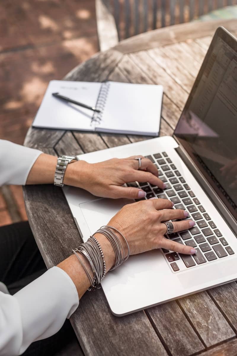 person typing on a laptop with an open notebook on the left