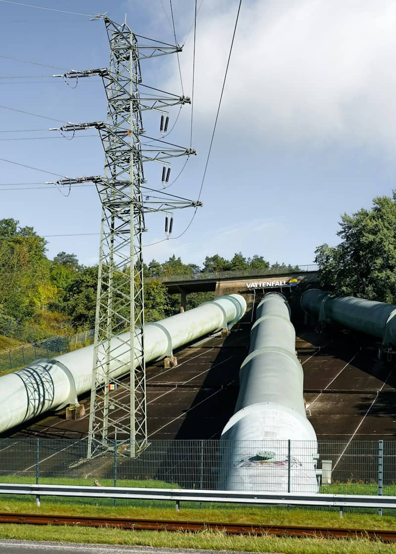 Large industrial pipes leading into a tunnel under a bridge with a power pylon