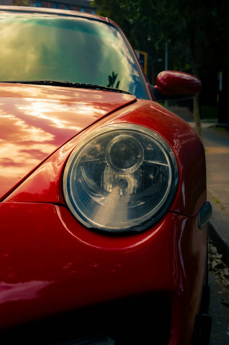 A red sports car headlight reflecting a cloudy sky at golden hour